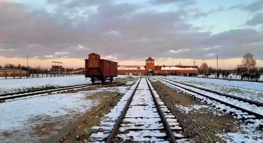 Zimowy krajobraz obozu Auschwitz z widocznym wagonem towarowym na torach, symbolem transportów do piekła.