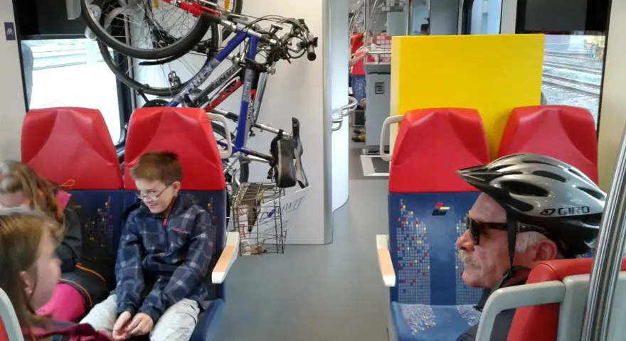 W pociągu Kolei Mazowieckich rowerzyści podróżują z rowerami. Dzieci i dorośli siedzą obok.