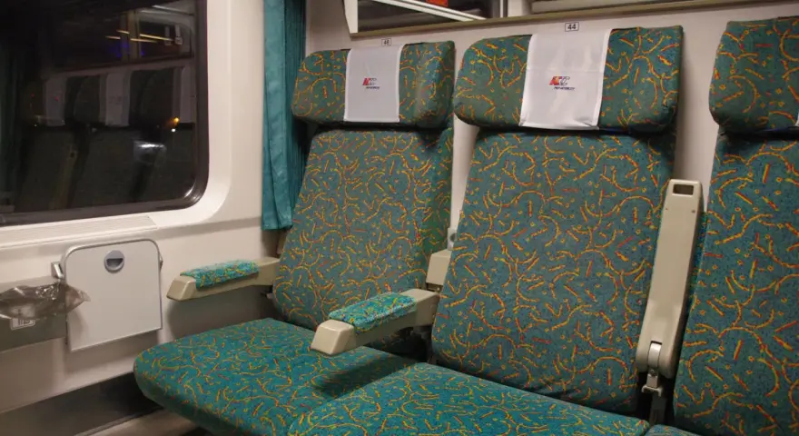 Wnętrze wagonu 4 Pendolino. Widok na dwa rzędy siedzeń z charakterystycznym wzorem.