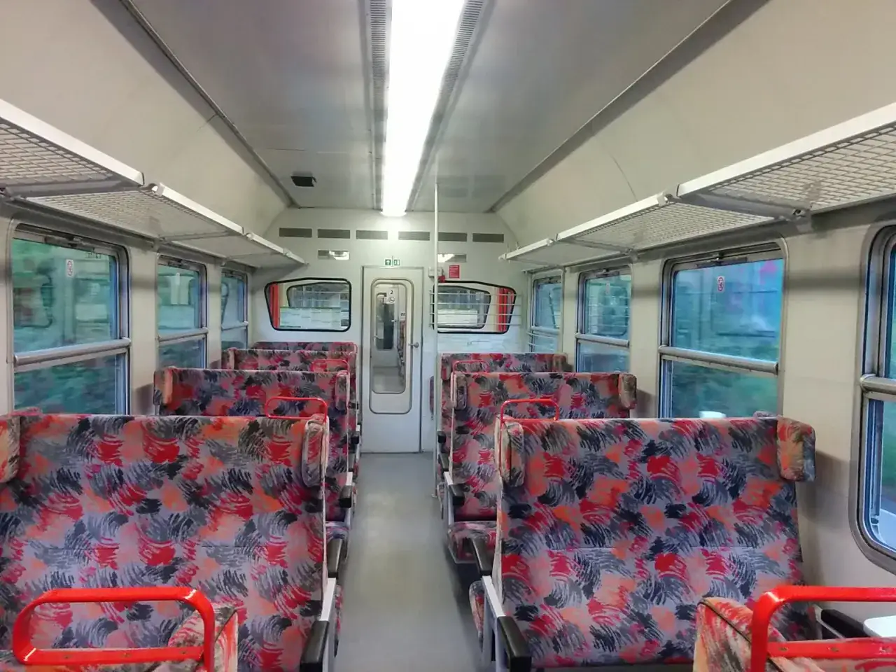Puste siedzenia w wagonie 1 klasa intercity. Kolorowe obicia foteli i duże okna.