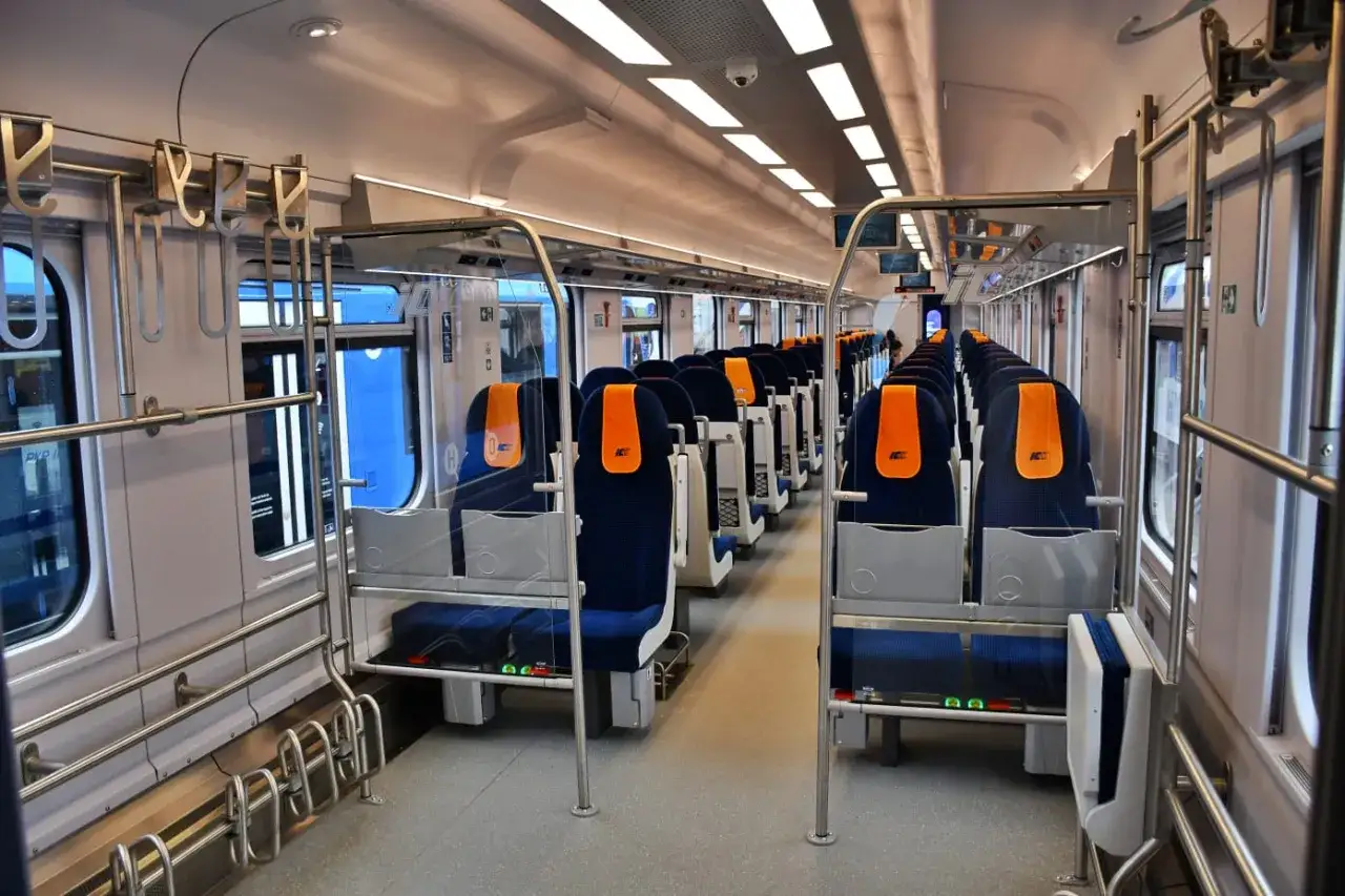 Wnętrze wagonu przedziałowego PKP Intercity z rzędami niebieskich siedzeń i pomarańczowymi zagłówkami.