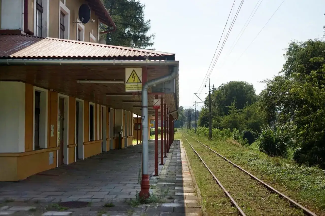 Dworzec Nowy Sącz. Peron zadaszony, tory kolejowe wiodą w dal. Rozkład jazdy pociągów czeka na podróżnych.