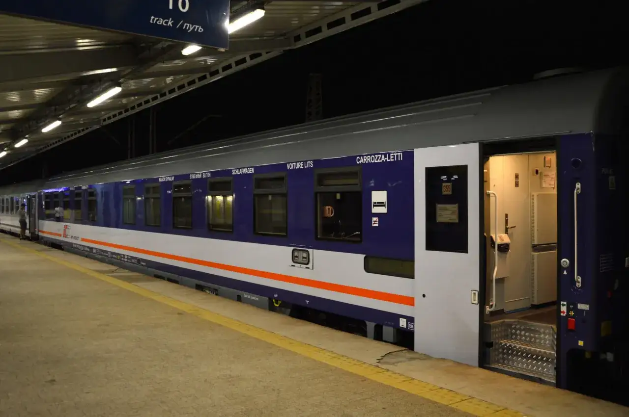 Nocny pociąg PKP Intercity z otwartymi drzwiami na peronie. Wagon sypialny z wielojęzycznymi napisami.