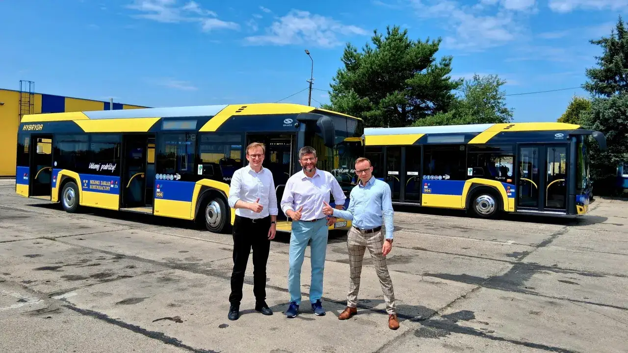Trzech mężczyzn pozuje przed nowymi autobusami hybrydowymi w Pabianicach. Miasto Łódź inwestuje w ekologiczny transport.