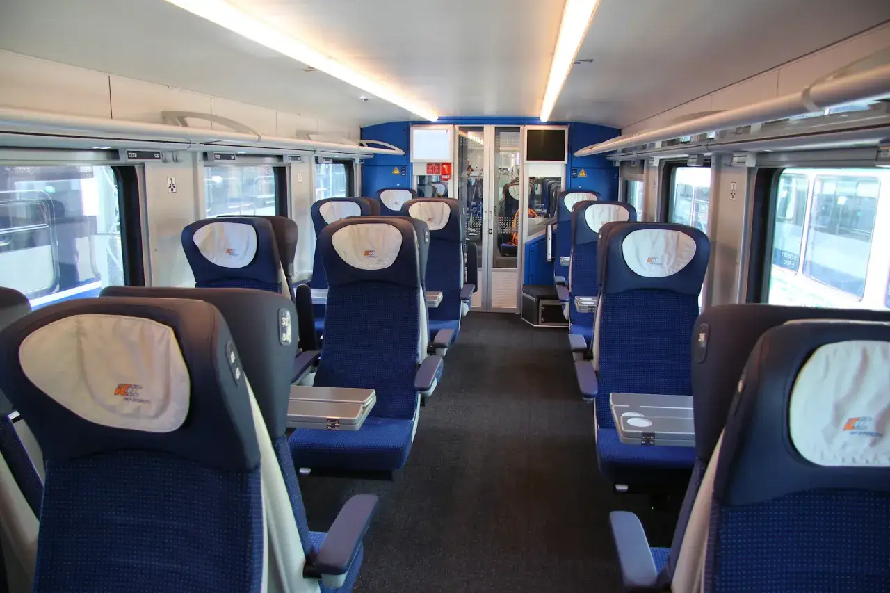 Wnętrze wagonu PKP Intercity ed160. Siedzenia w kolorze granatowym z białymi zagłówkami, stoliki, okna.