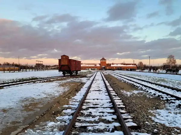 Zimowy krajobraz obozu Auschwitz z widocznym wagonem towarowym na torach, symbolem transportów do piekła.