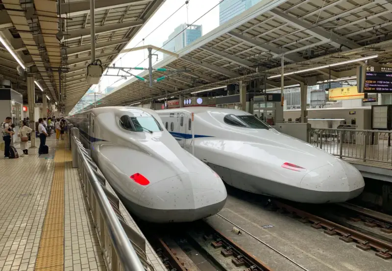 Dwa białe pociągi Shinkansen stojące na peronie, gotowe do podróży.